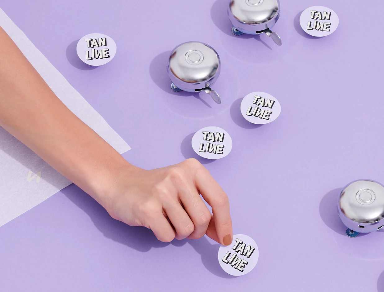 Hand placing round white custom labels on silver tins on a lilac surface