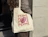 Person carrying a natural cotton tote bag with a red lettering and rose print over the shoulder