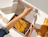 Top-down view of hands peeling the adhesive protective strip from a white shipping box filled with brown paper shred and yellow suede gloves