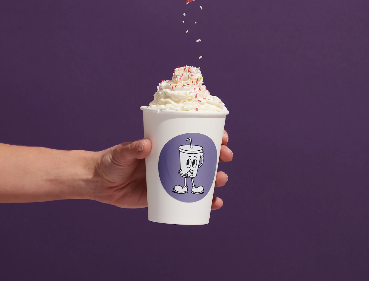 Hand holding a paper cup with a round purple illustrated custom label