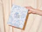 Hand holding a white eco colour mailer box with a full blue botanical pattern print