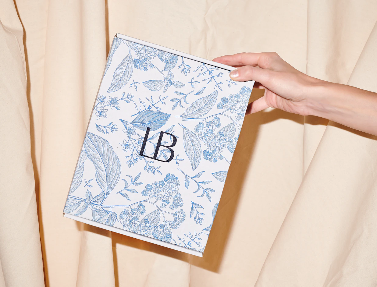 Hand holding a white eco colour mailer box with a full blue botanical pattern print
