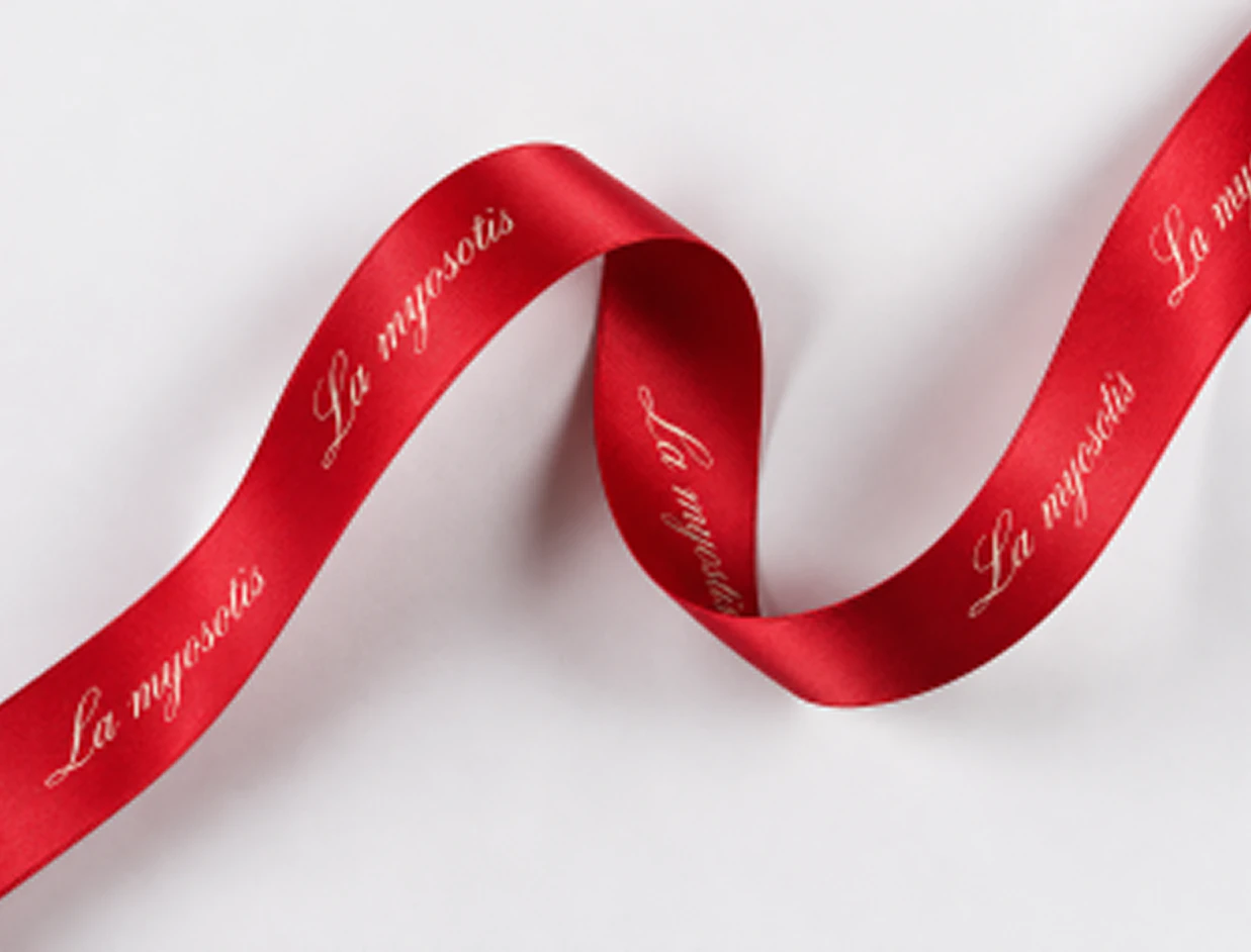 A red satin ribbon printed with 'La myosotis' cursive typography curling across a white background