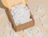 A cardboard shipping box overflowing with white eco-friendly packing peanuts against a beige background