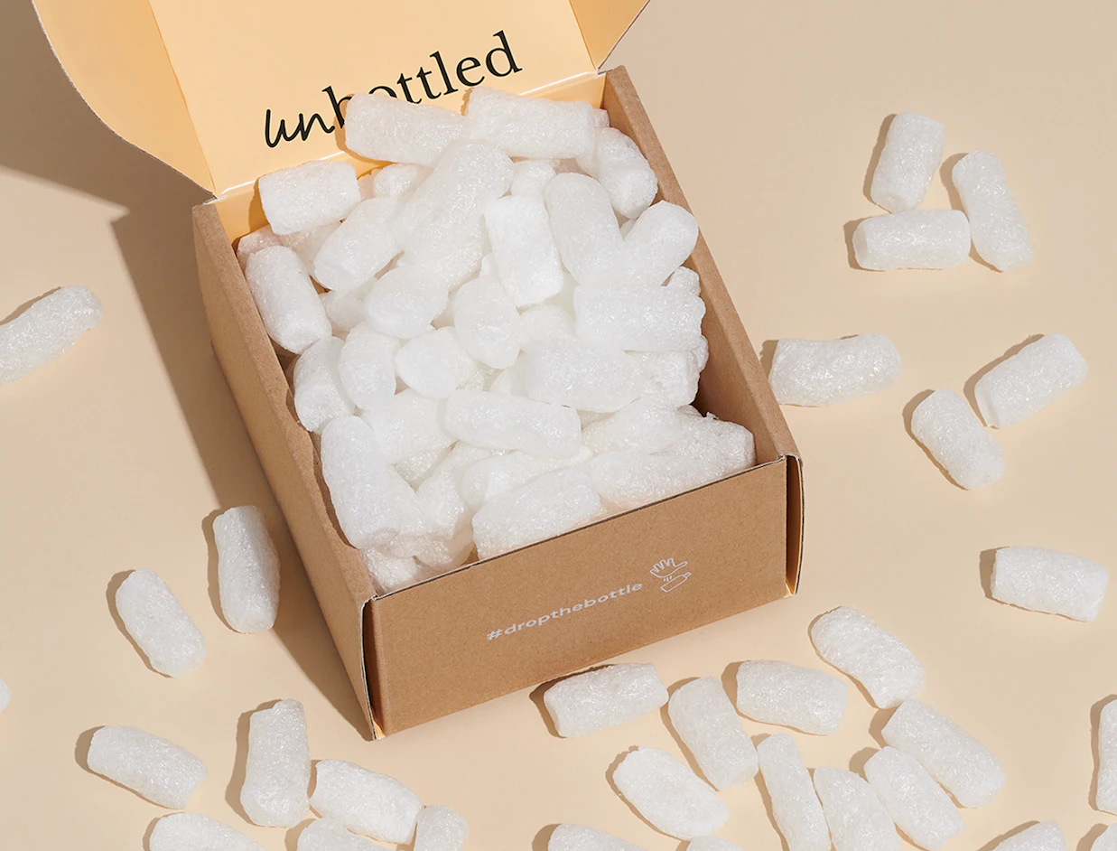 A cardboard shipping box overflowing with white eco-friendly packing peanuts against a beige background