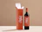 A bottle of red wine standing next to an open terracotta-orange wine box with matching white typography