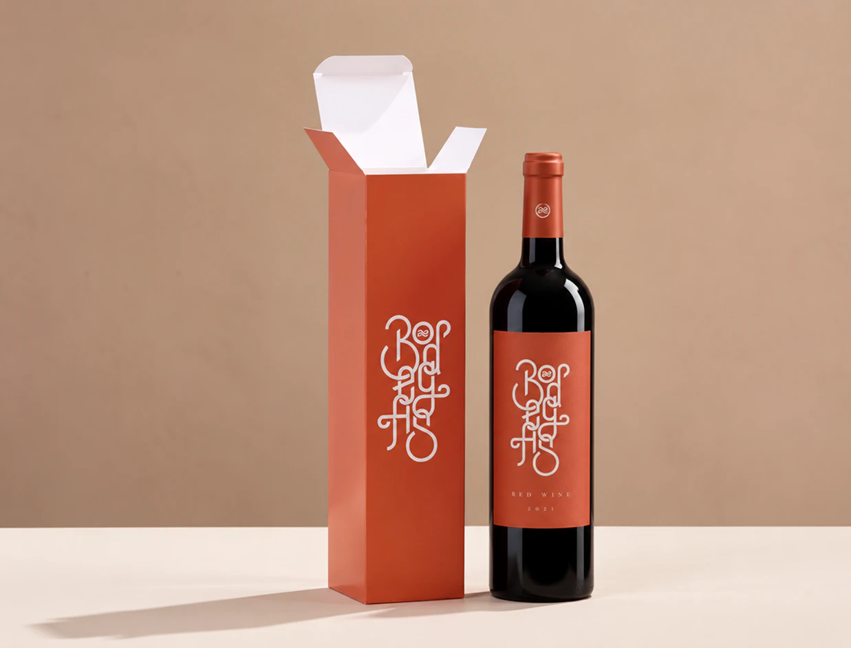 A bottle of red wine standing next to an open terracotta-orange wine box with matching white typography