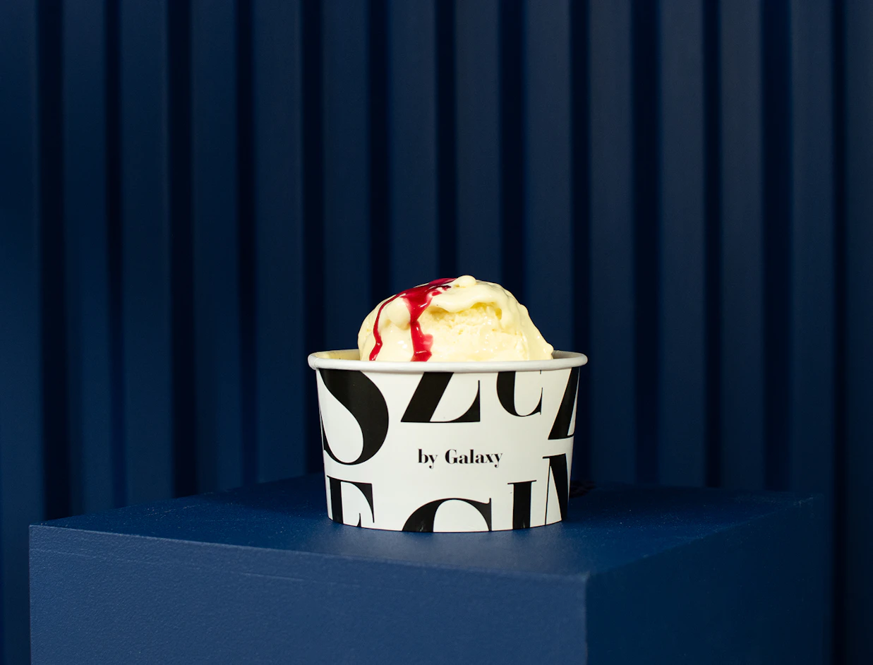 A white paper cup with black typography filled with vanilla ice cream and berry sauce on a blue pedestal