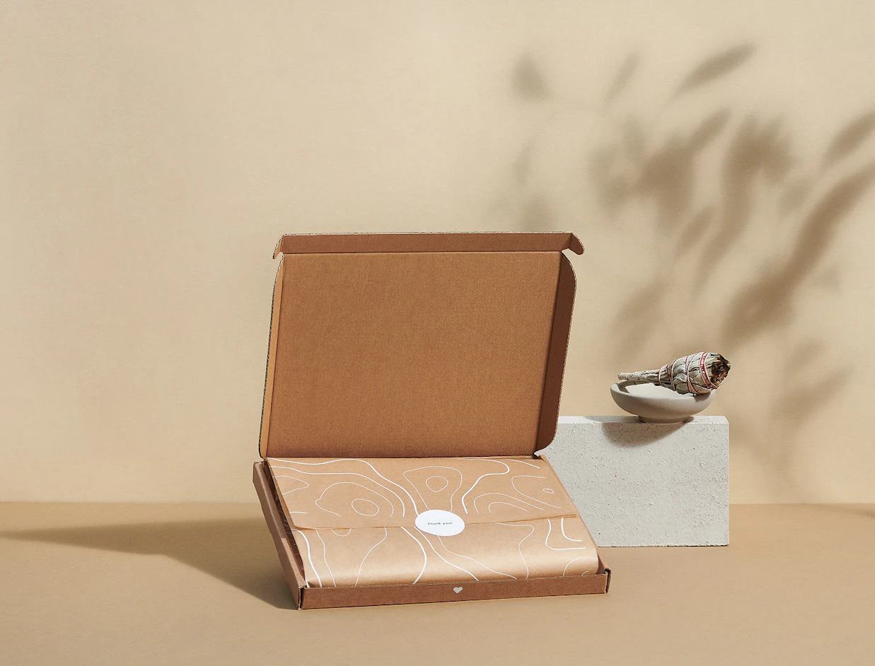 An open cardboard box containing items wrapped in brown tissue paper sealed with a 'Thank you' sticker