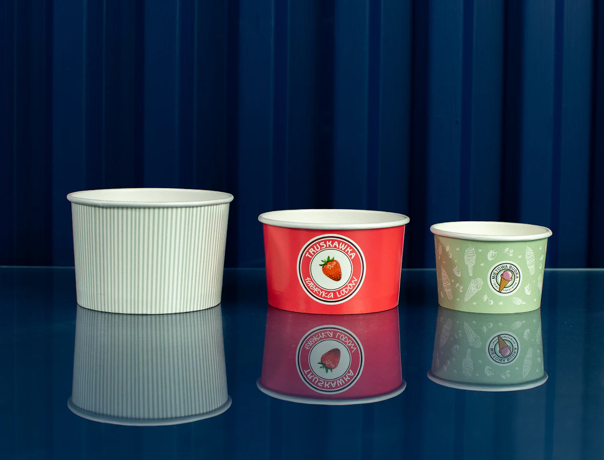 Three ice cream paper cups in different sizes and designs lined up on a reflective blue table