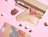 Crafting setup with rolls of abstract patterned wrapping paper, candles, and a face ceramic pot on a pink background