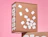 Kraft mailer box with bold white lettering and scattered white shapes, on a pink background