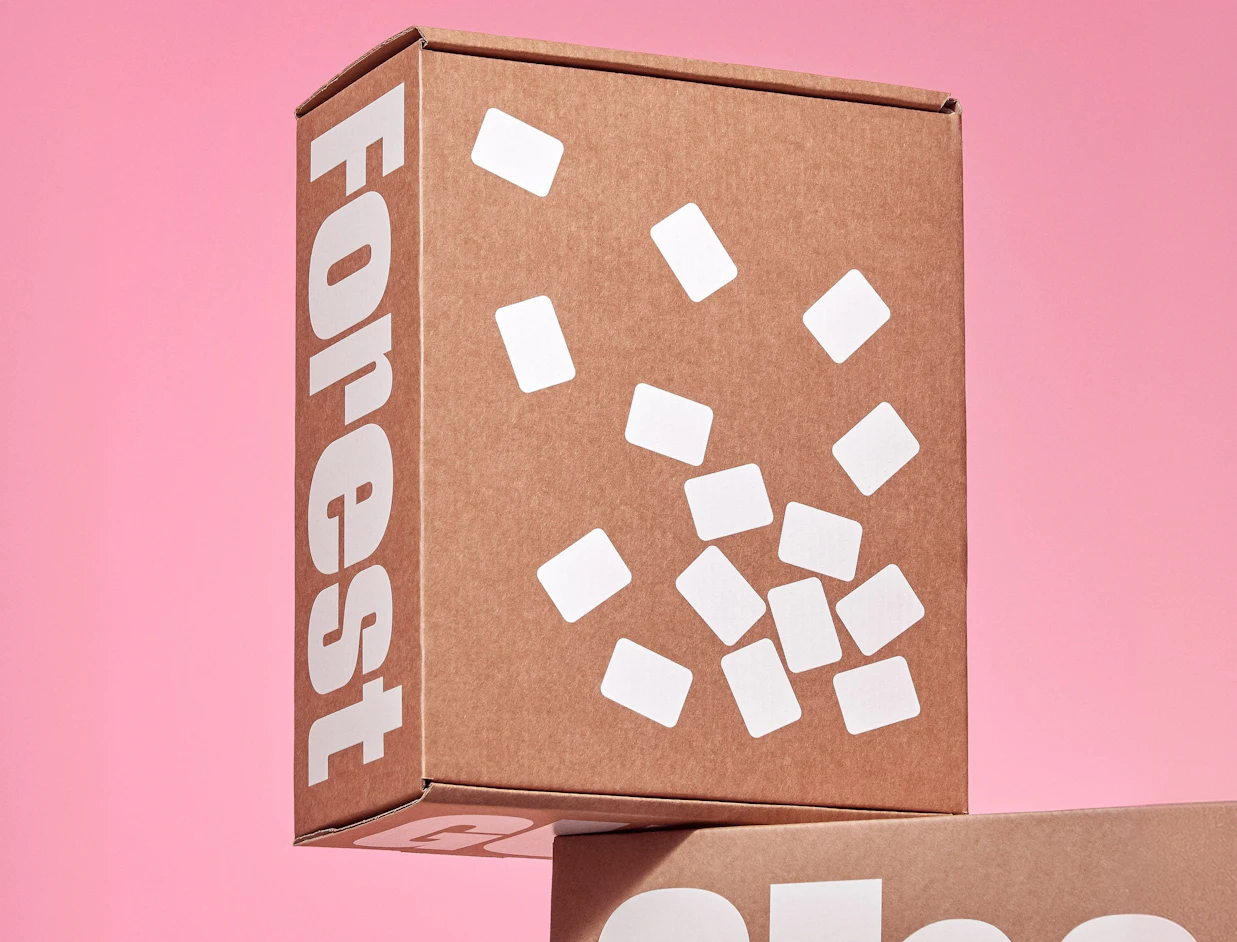 Kraft mailer box with bold white lettering and scattered white shapes, on a pink background