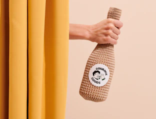 Hand holding a knit-covered bottle with a round white custom label