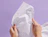 Hands holding crumpled white tissue paper with a subtle print on a lilac background