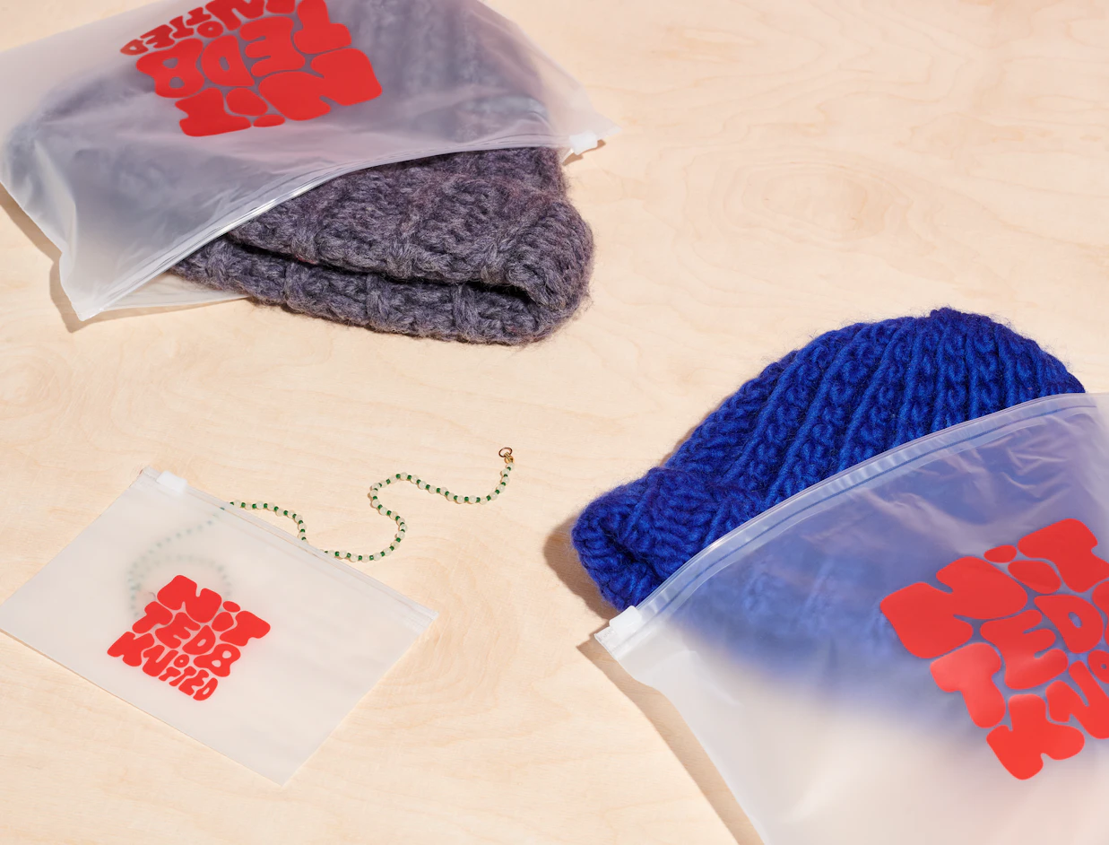 Frosted zipper bags with a red logo print holding knit beanies