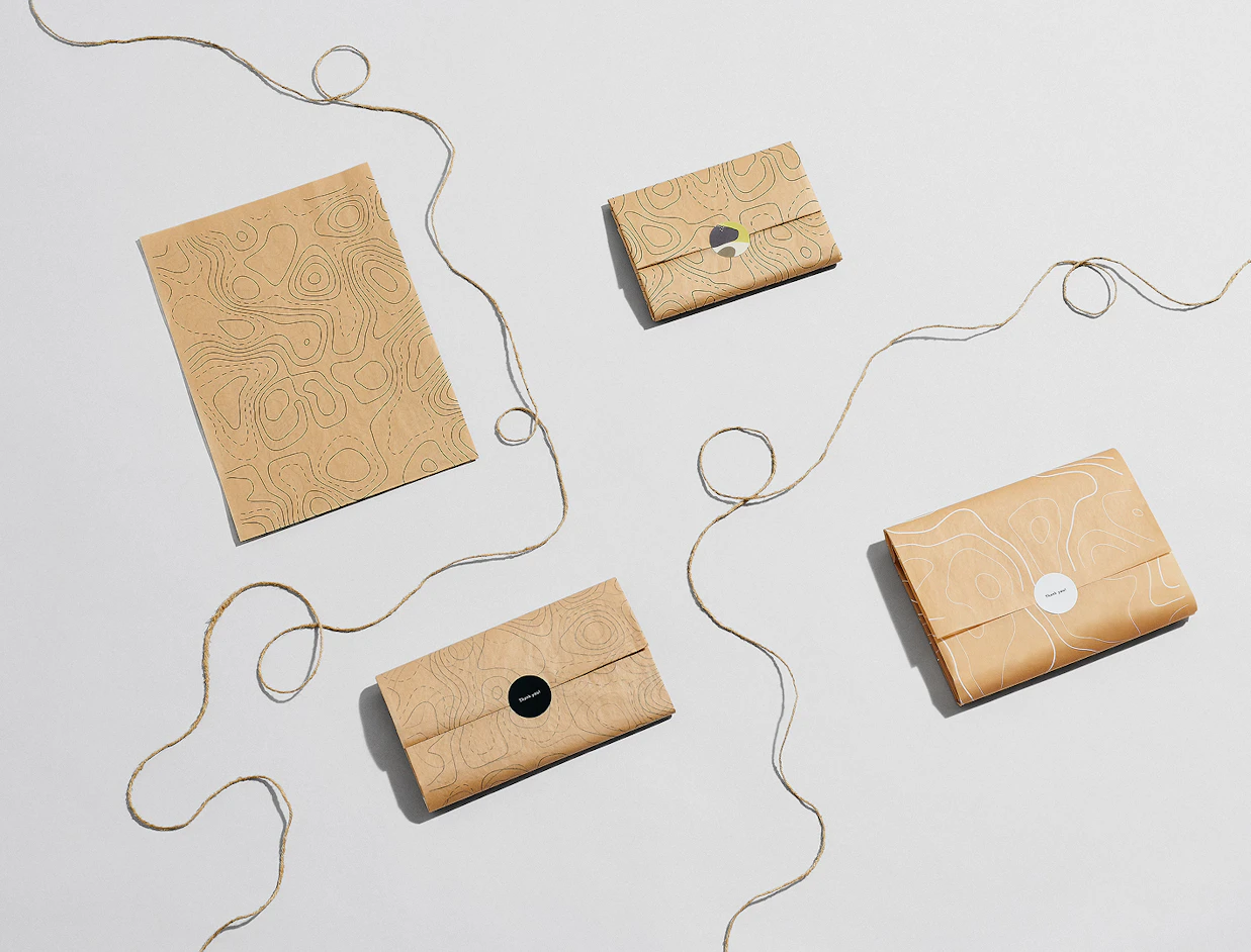 Top-down view of several gifts wrapped in brown topographic-patterned paper and sealed with stickers, laid out with jute twine