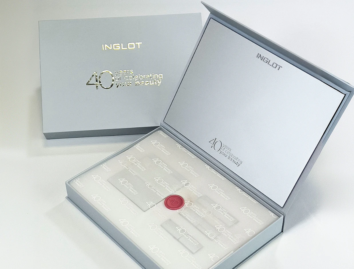 An open grey rigid presentation box branded 'INGLOT 40 years of celebrating your beauty' with custom branded tissue paper and a red wax seal