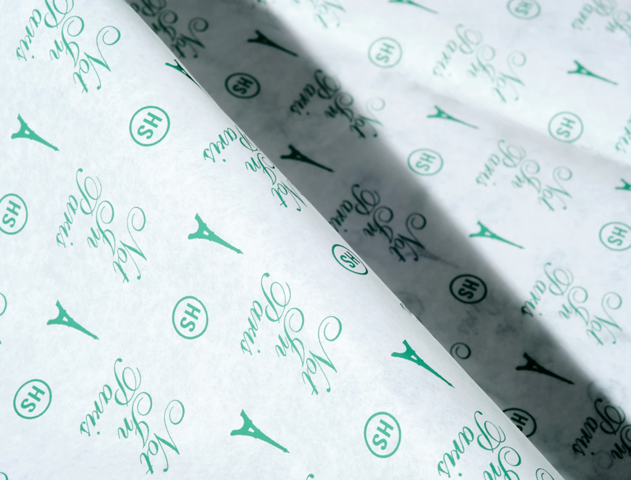 Close-up of white tissue paper with a green repeat pattern of icons and script lettering