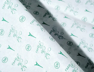 Close-up of white tissue paper with a green repeat pattern of icons and script lettering
