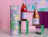 Tall paper can with a colourful gradient print next to wine bottles on a green stand