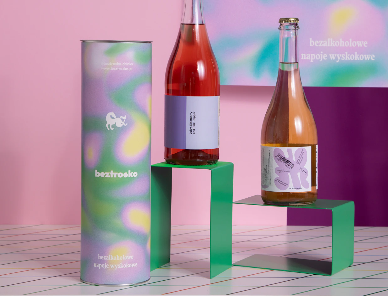 Tall paper can with a colourful gradient print next to wine bottles on a green stand