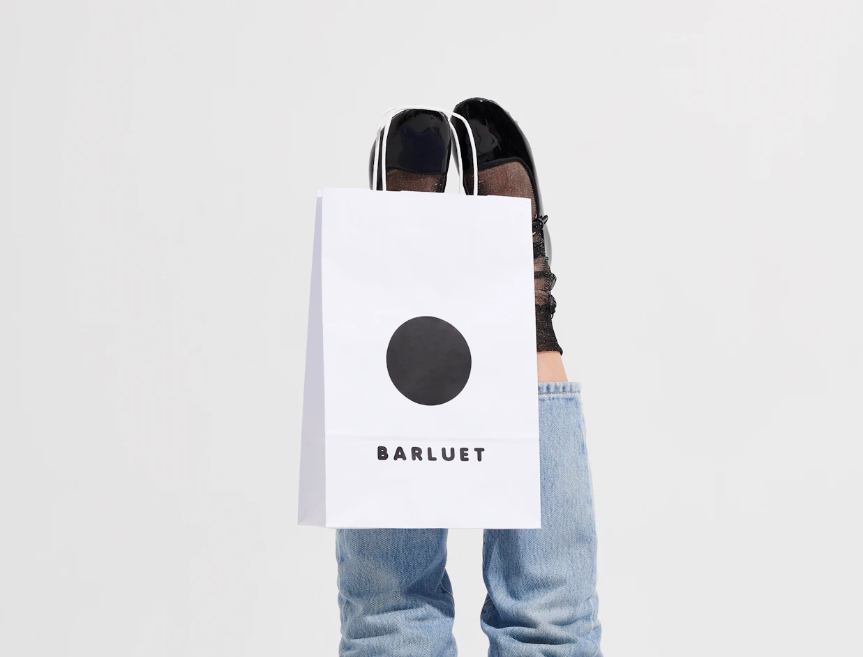 White printed paper bag with a black circle logo held in front of a person