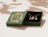 An open dark green jewelry box with gold foil palm leaf details displaying a necklace and matching earrings set