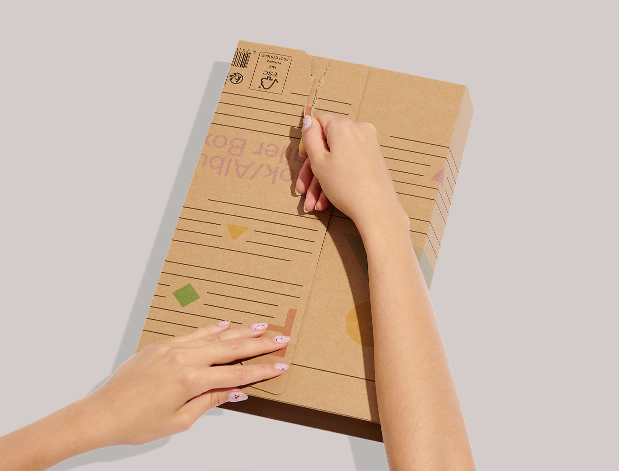 Hands opening a sealed kraft cardboard book mailer using the integrated tear strip
