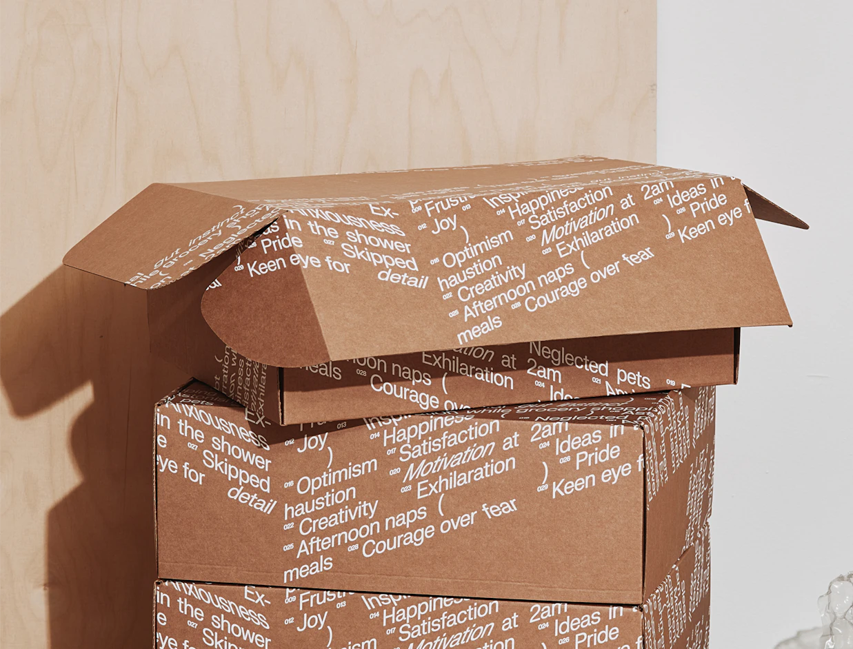 Stack of kraft mailer boxes with an all-over white text print, the top box open