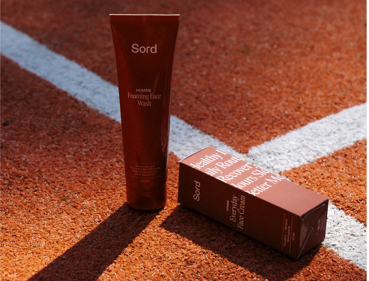A brown tube of Sord Foaming Face Wash standing next to its box on an orange running track