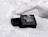A small open black jewelry box holding a clear glass flower ring, placed on crumpled white polka-dot tissue paper