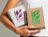 A person holding two small 'Linoã' shipping boxes, one white with purple metallic foil and one craft brown with green metallic foil