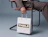 A person in a suit seated on a chair holding a white paper shopping bag with 'THALE' printed on a green block