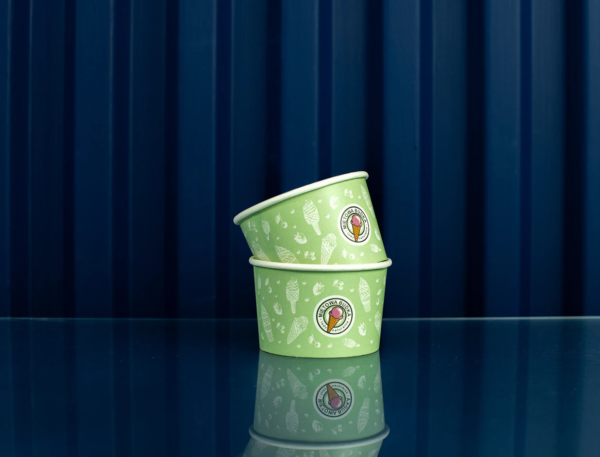 Two stacked green paper ice cream cups printed with ice cream illustrations and 'Miętowa Budka' logo against a blue background