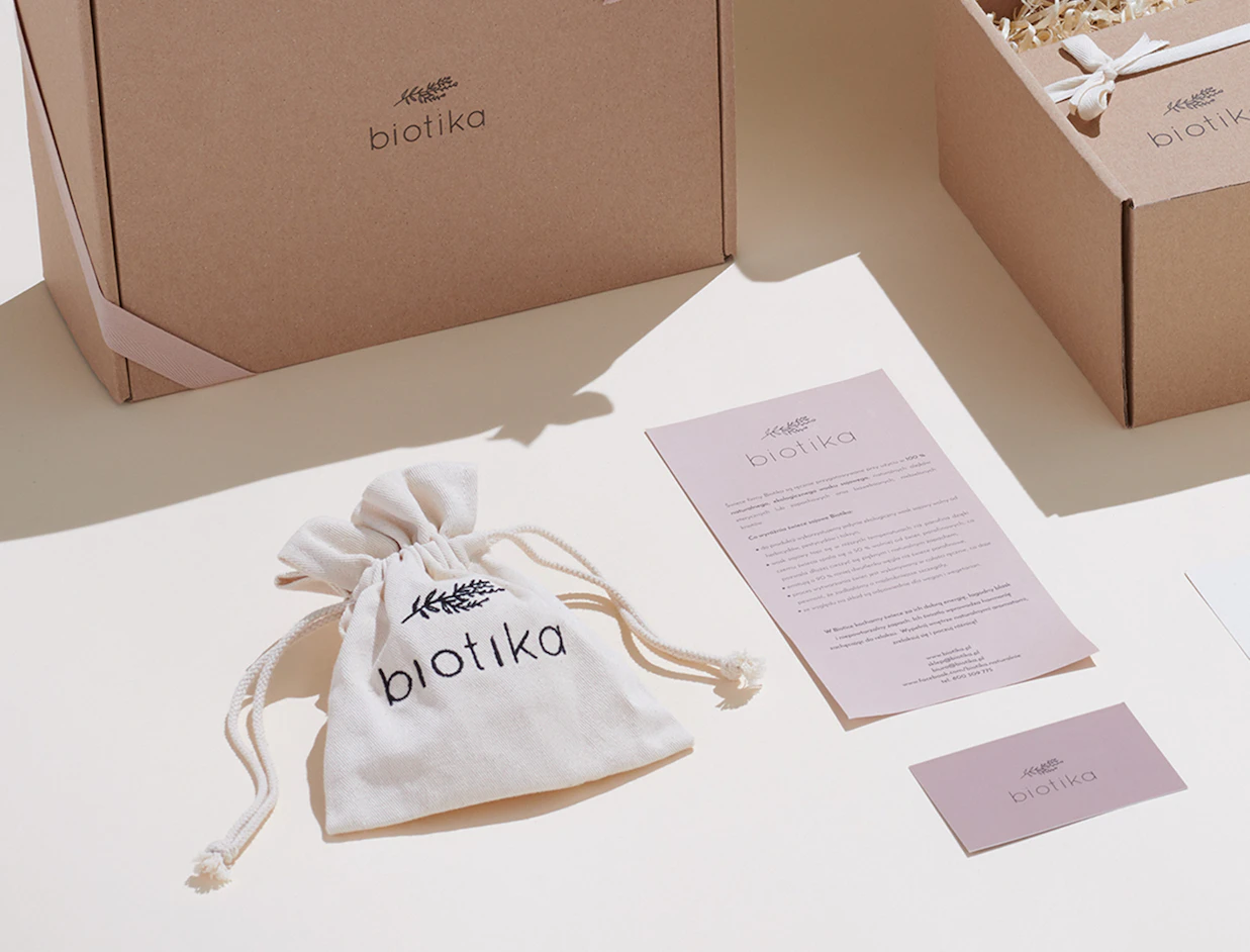 A small white cotton drawstring bag printed with 'biotika' next to brand information cards and cardboard shipping boxes