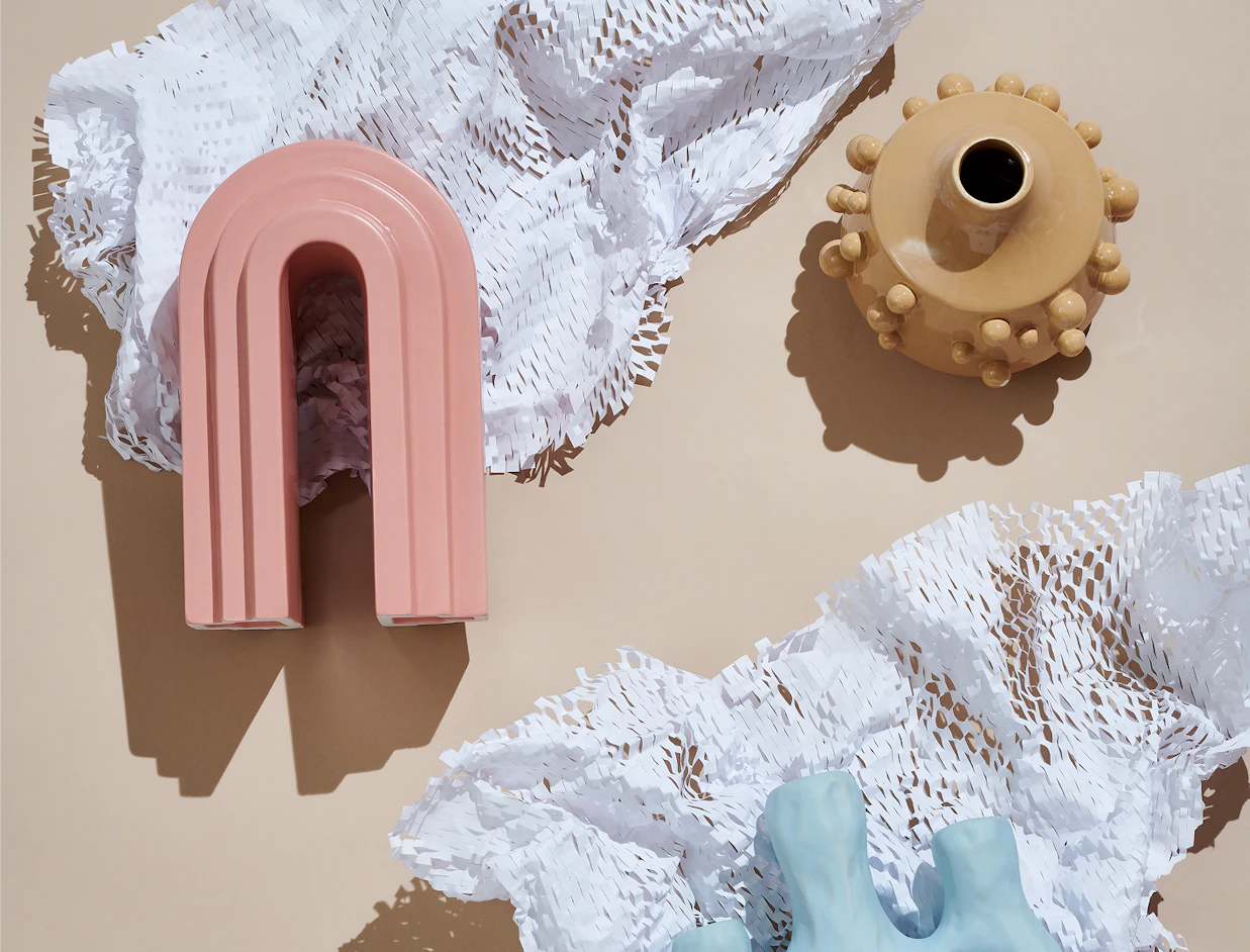 Top-down view of modern ceramic vases placed among white protective honeycomb paper on a beige background