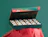 An open festive advent box filled with small glass jars with QR codes on red lids, set on red tissue paper
