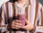 A person wearing a brown and purple striped shirt holding a clear plastic cup filled with a berry smoothie branded with 'Nuts'