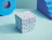Light blue cube gift box decorated with colorful illustrated human figures, placed between blue geometric prop shapes