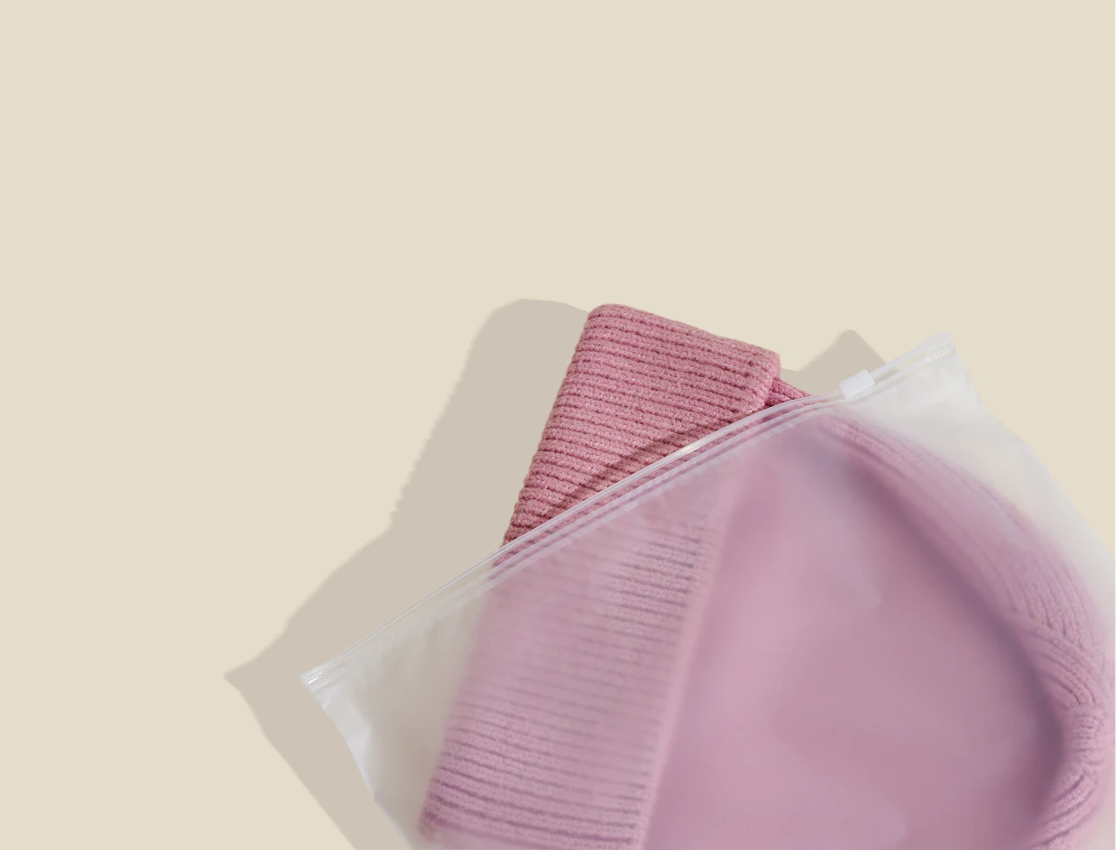 Frosted zipper bag holding a pink knit beanie on a beige background