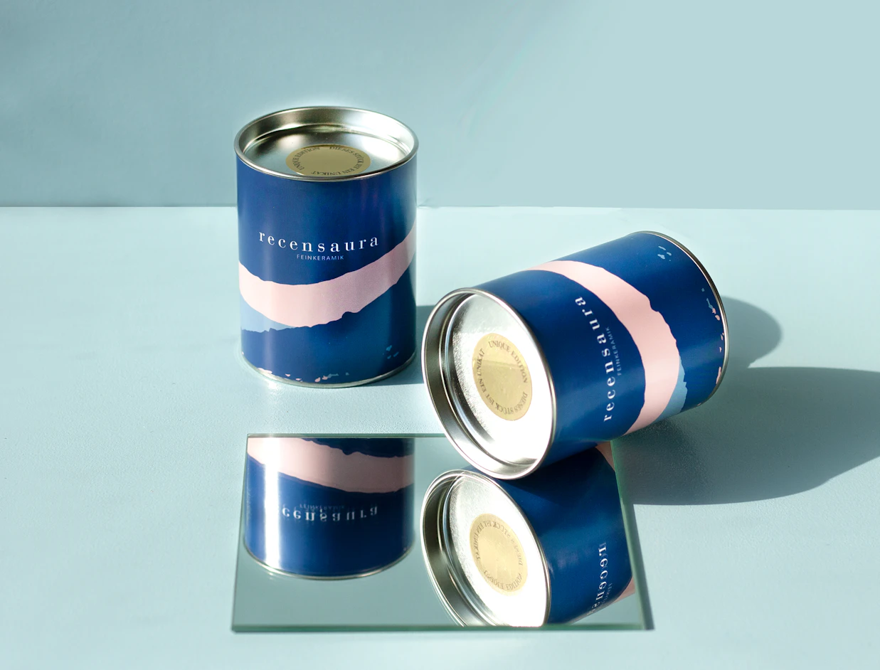 Navy and pink printed paper cans with metal ends, one lying on a mirror