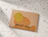 A brown craft envelope printed with abstract mustard-yellow shapes and the text 'RSVP Yes!' on a terrazzo surface