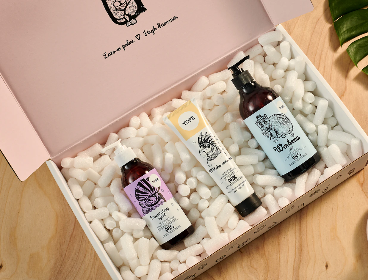 An open pink gift box filled with white biodegradable packing peanuts protecting three Yope bath and body products