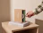 A hand opening a kraft sliding drawer box branded 'ÉCLAT JEWELRY' resting on a stack of books on a wooden nightstand