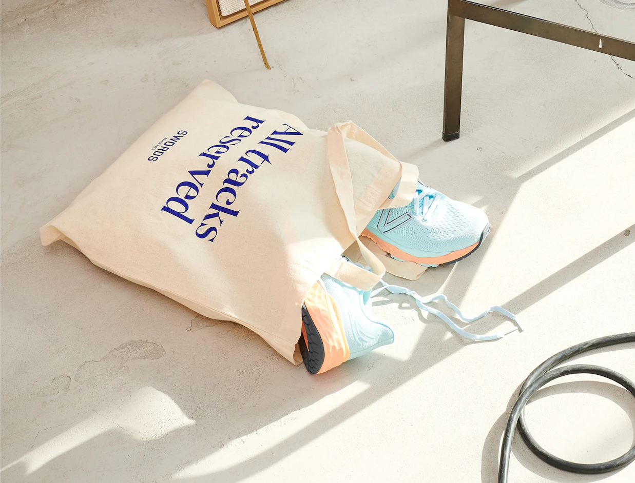 Natural cotton tote bag with a navy text print lying on the floor with sneakers inside