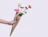 A hand holding a flower bouquet wrapped in brown paper with black wavy lines on a plain light background