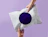 Two hands holding a white poly mailer with a large dark purple circle printed in the center against a light purple background