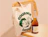 Natural cotton tote bag with a green illustrated logo print, hanging on a rattan chair