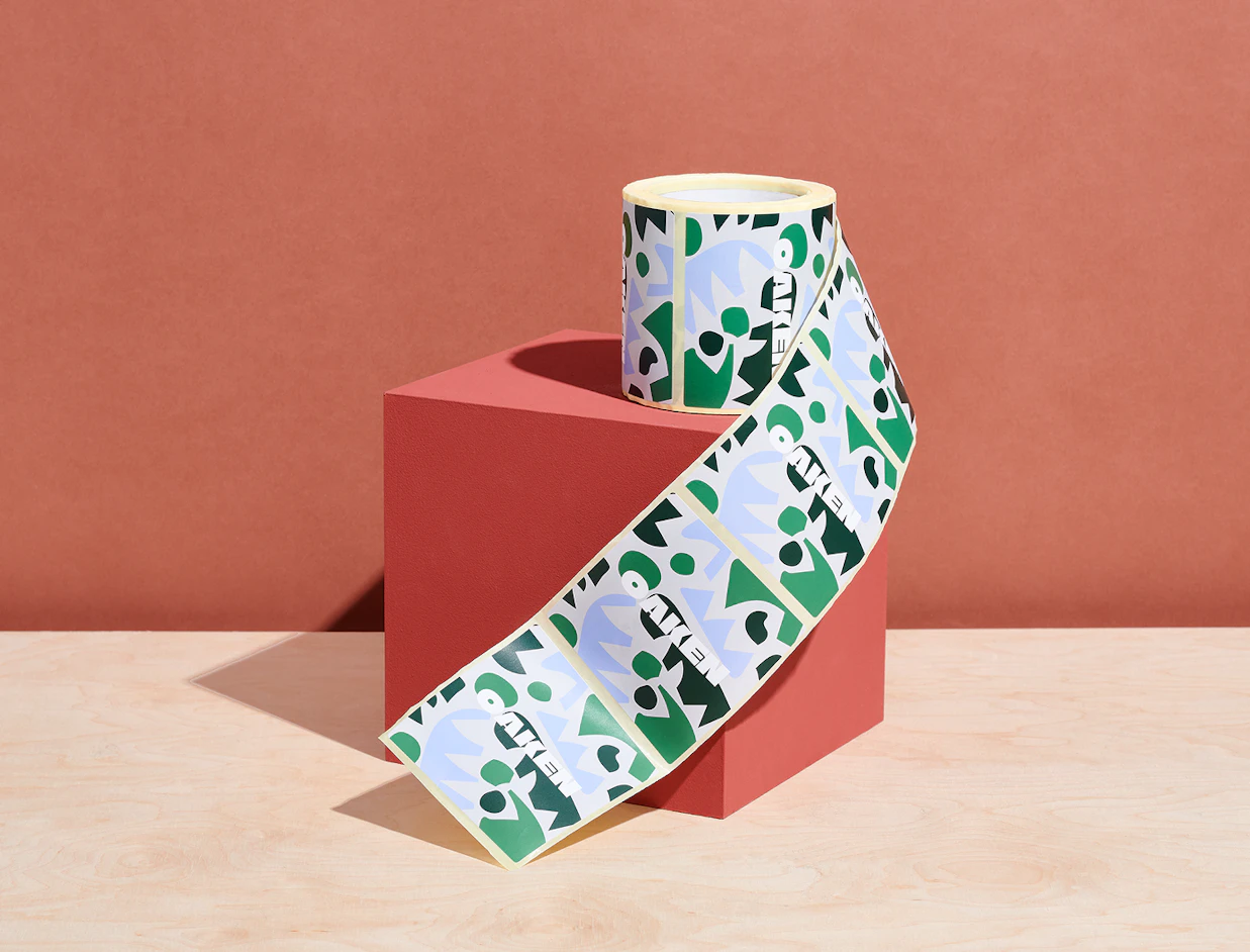A roll of custom labels with abstract green and blue patterns unrolling over a red cube